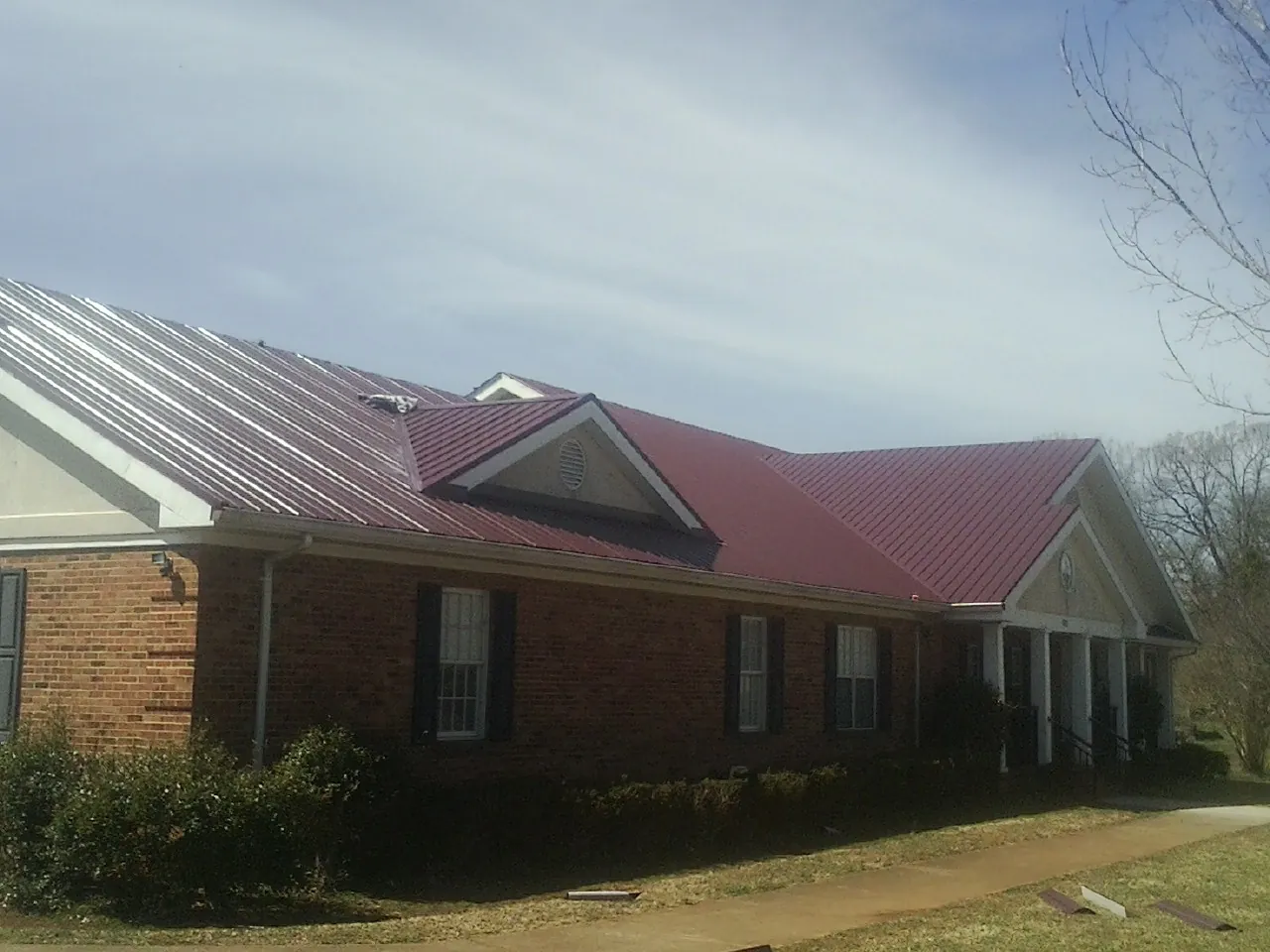 Red metal roof with gabled entries on a long brick building, from a Hail Damage Roof Repair job in Genesee