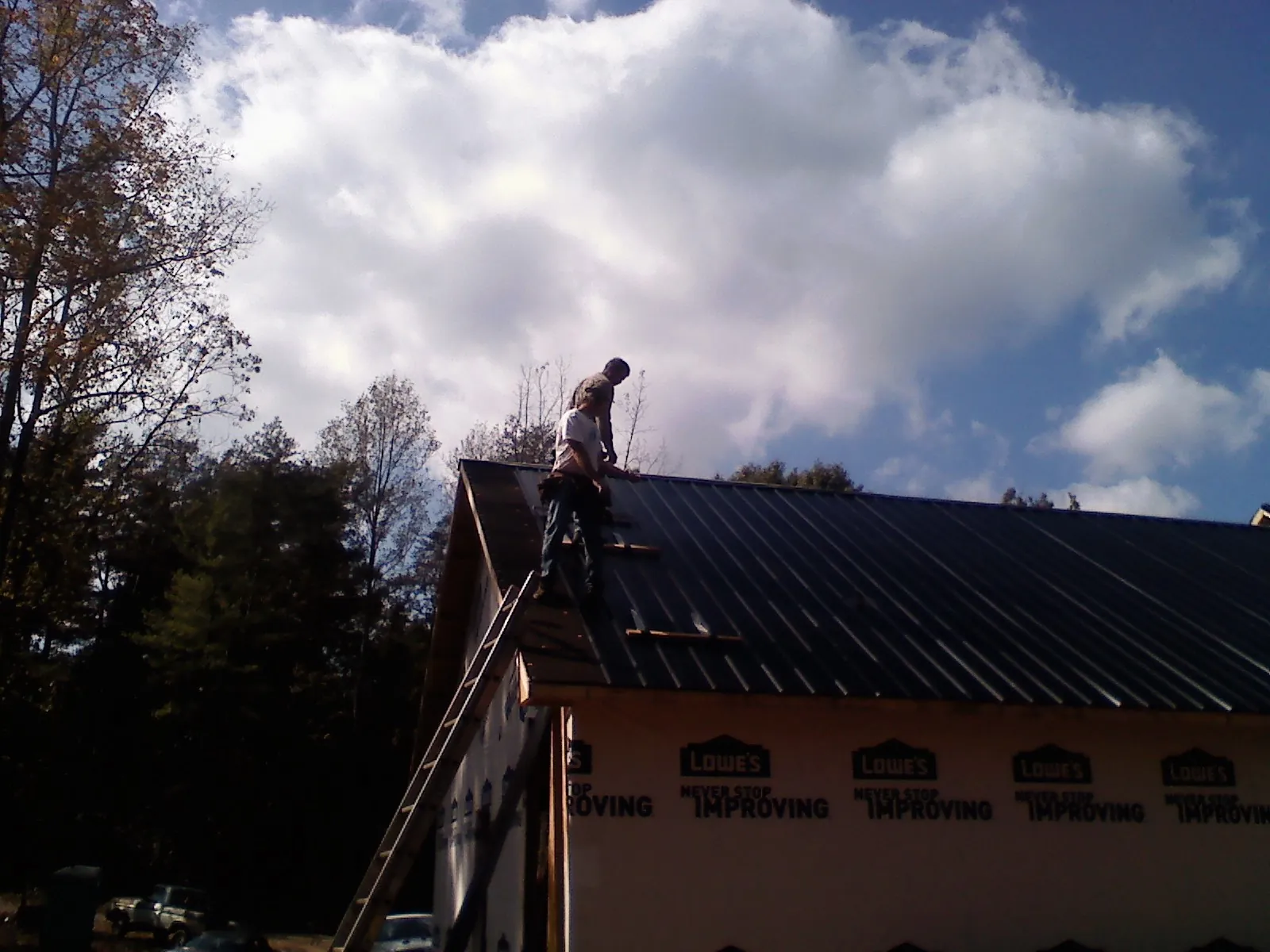 Roofer fastening dark metal panels high against a cloudy sky, from a Roof Inspection job in Genesee