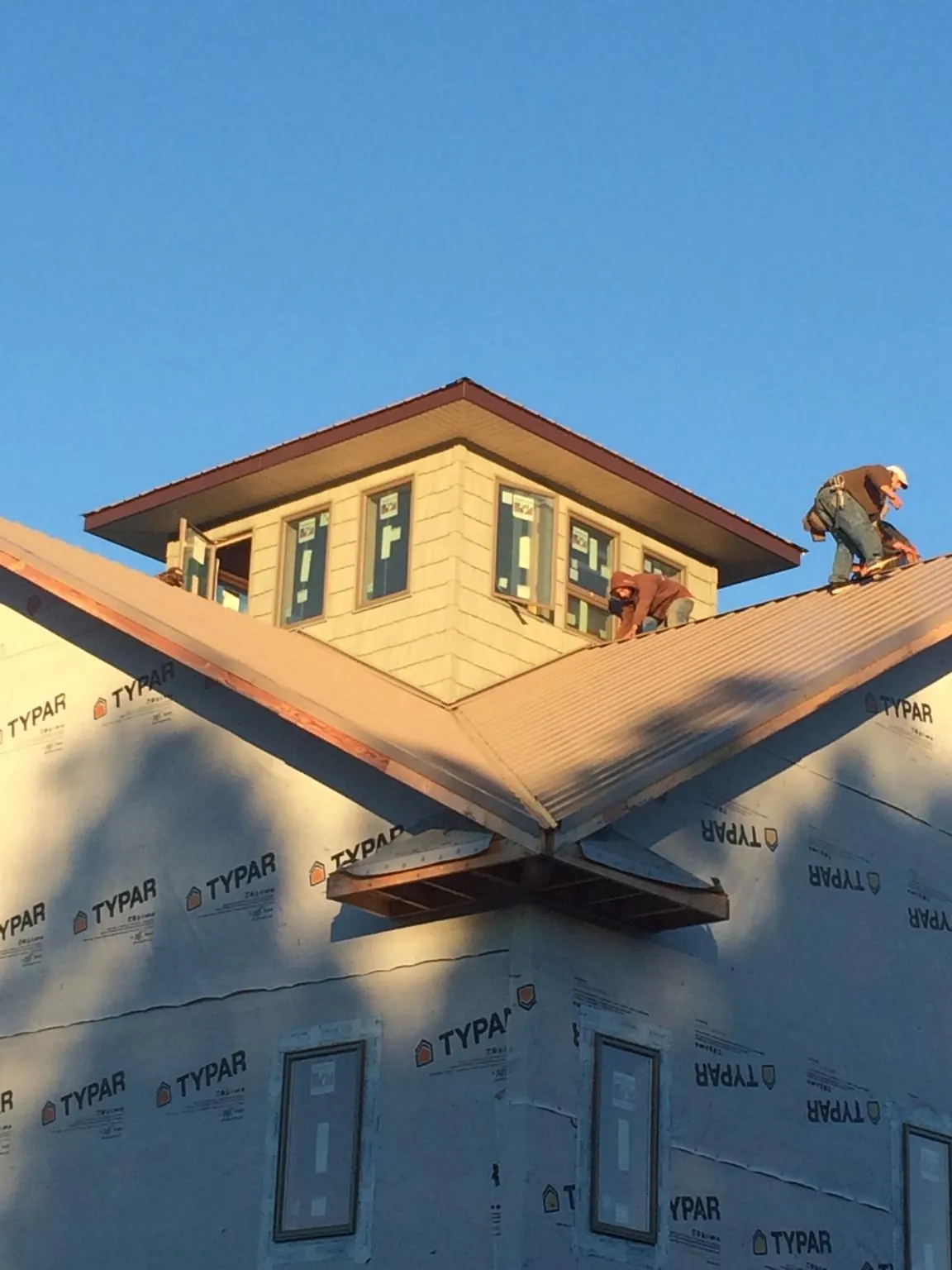 Roofers working around a rooftop cupola on a new metal roof at sunset — Roof Waterproofing in Genesee by Roofing Brothers